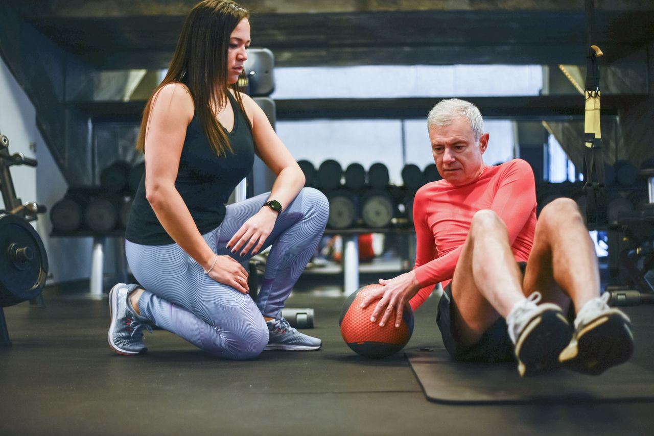 A senior man exercising with a personal trainer in a gym, focusing on core workouts.